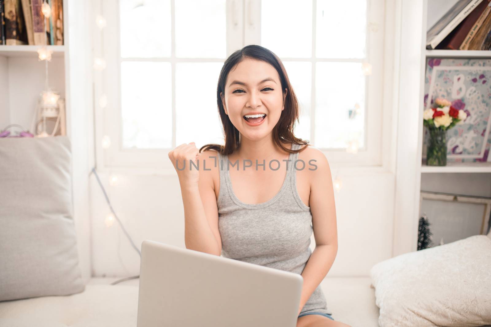 Happy excited asian young woman working on a laptop at home. by makidotvn