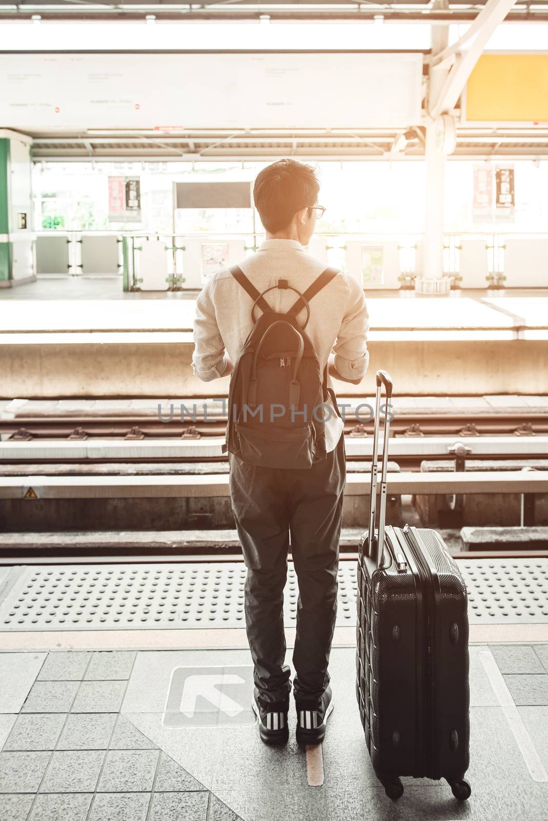 Man is on the train station with travel bag, using mobile phone, wait for a train