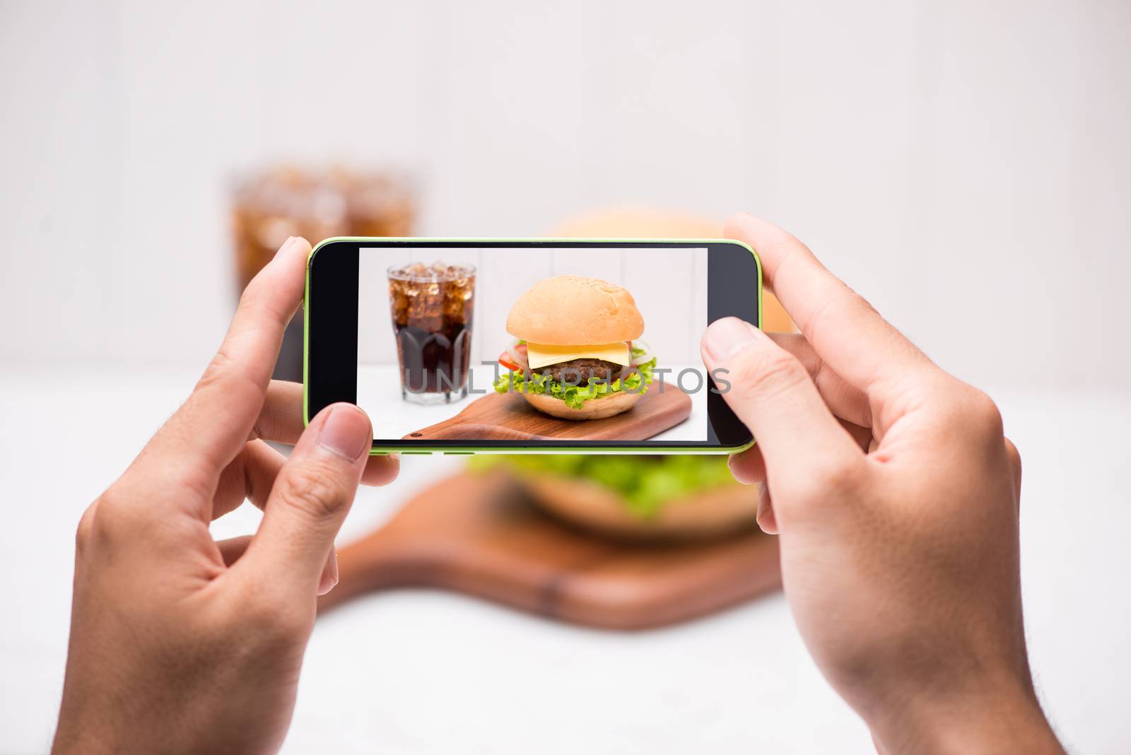 Hands hold smartphone taking photo of homemade BBQ burger
