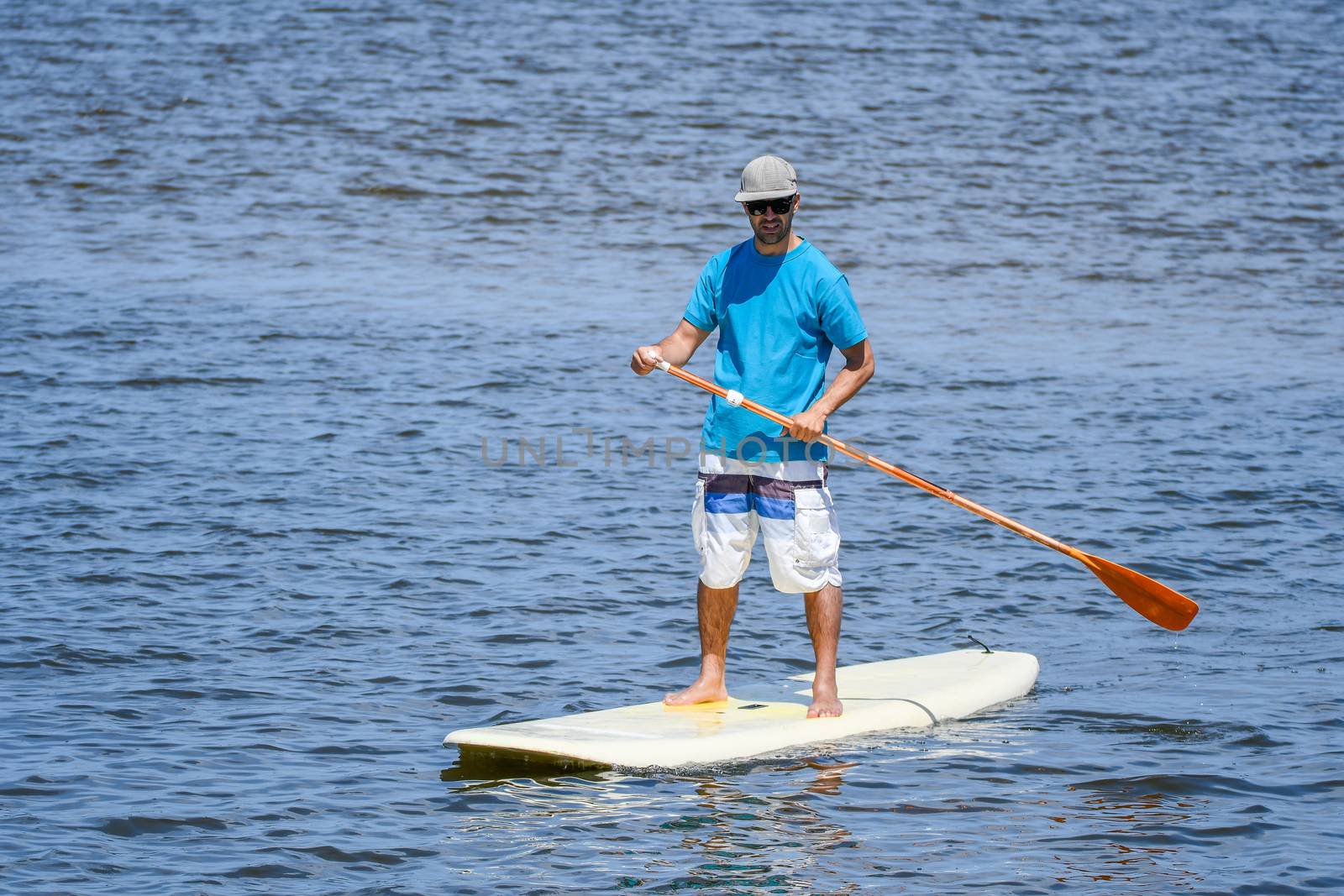 Man stand up paddleboarding on lake. Young man doing watersport on lake. Male tourist in swimwear during summer vacation.