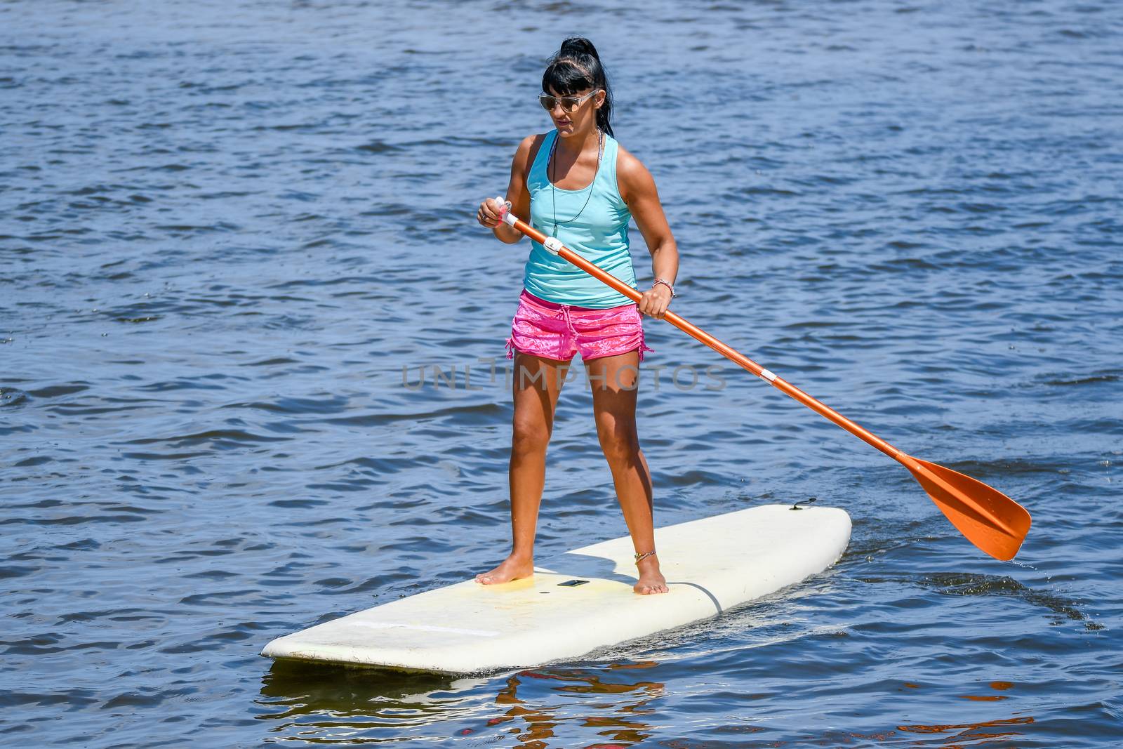 Woman stand up paddleboarding on lake. Young girl doing watersport on lake. Female tourist in swimwear during summer vacation.
