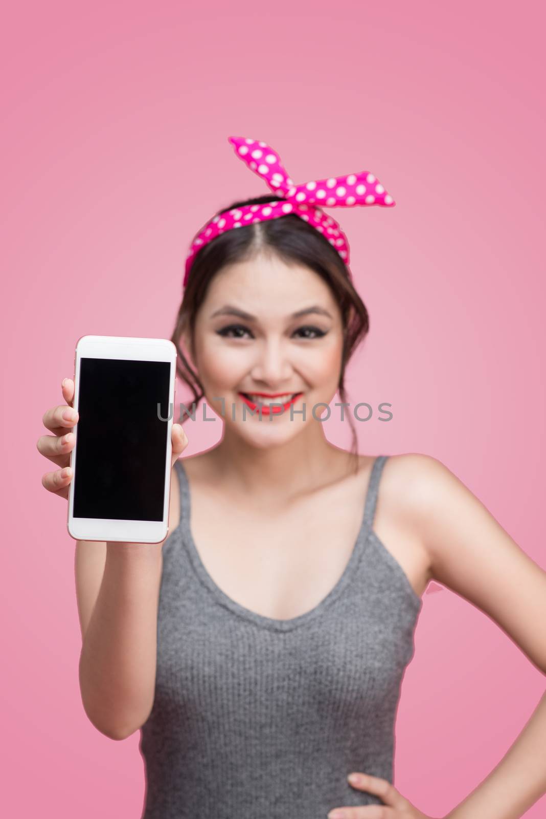 Beautiful young asian woman with pin-up make-up and hairstyle over pink background with mobile phone
