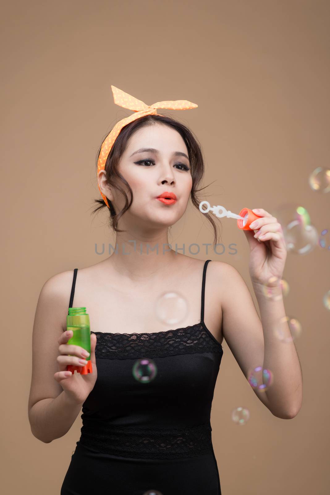 Playful pinup girl blowing party bubbles over yellow background