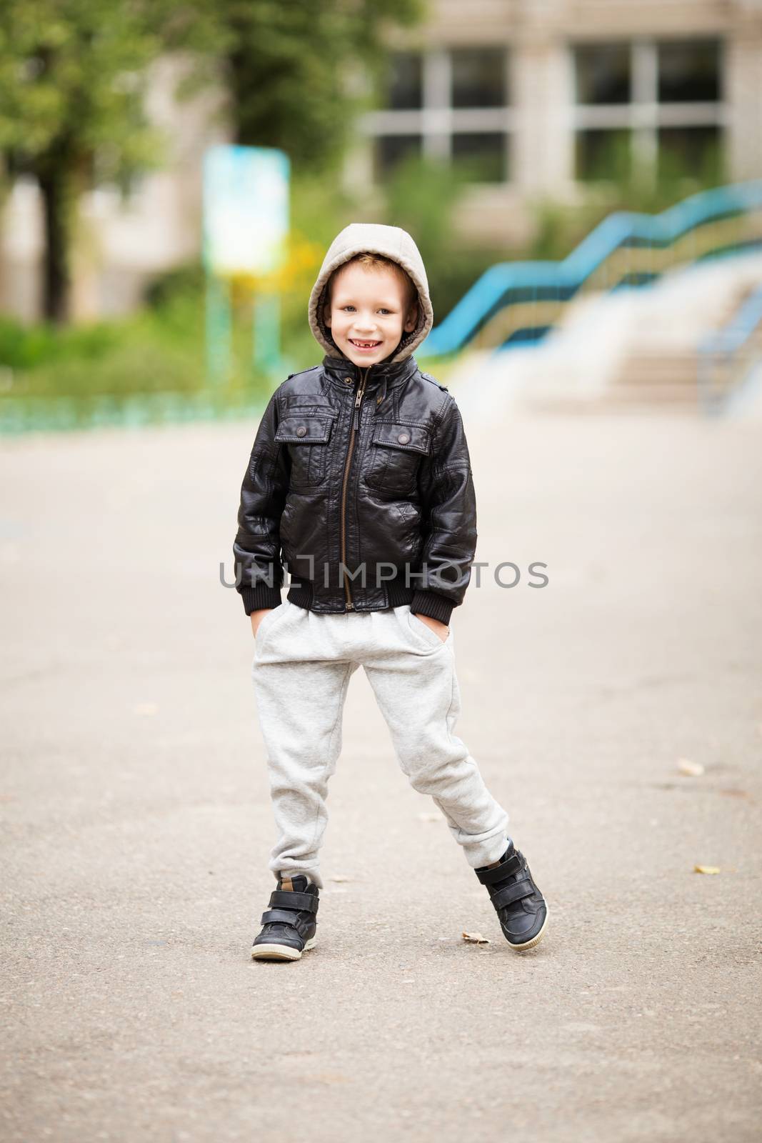 Full-length portrait of adorable little boy wearing black leather jacket. Urban kids. Hands in pockets. Loss of primary teeth in children.