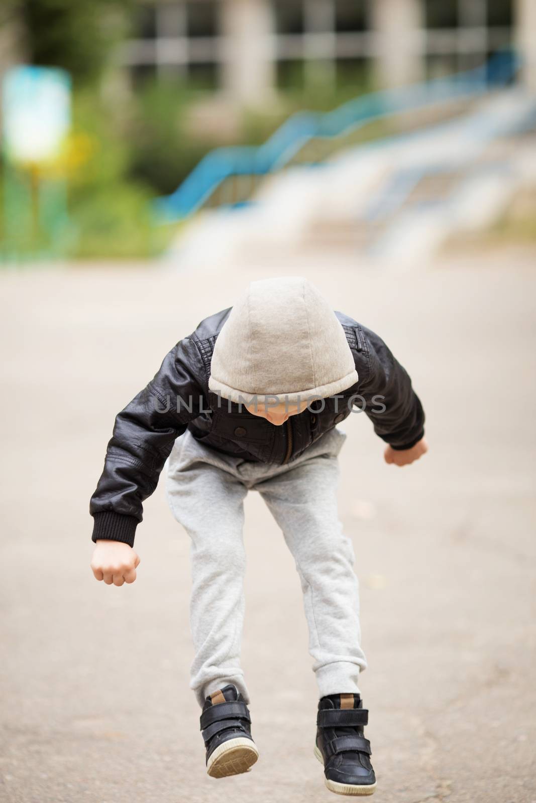 Full-length portrait of adorable little urban boy wearing black leather jacket. City style. Urban kids. Kid jumping and having fun outdoors