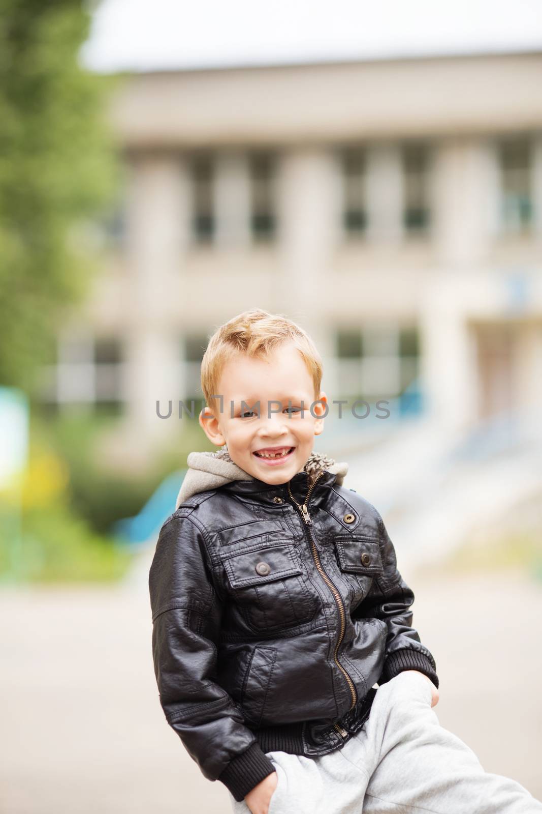 portrait of adorable little boy wearing black leather jacket. Urban kids. Hands in pockets. Loss of primary teeth in children.