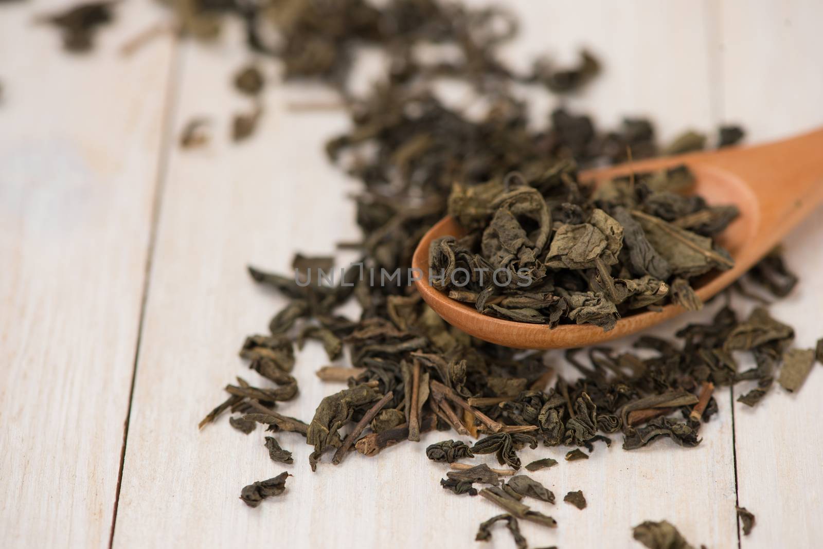 Black tea in a glass cup and tea leaves in wooden spoon on black stone background.