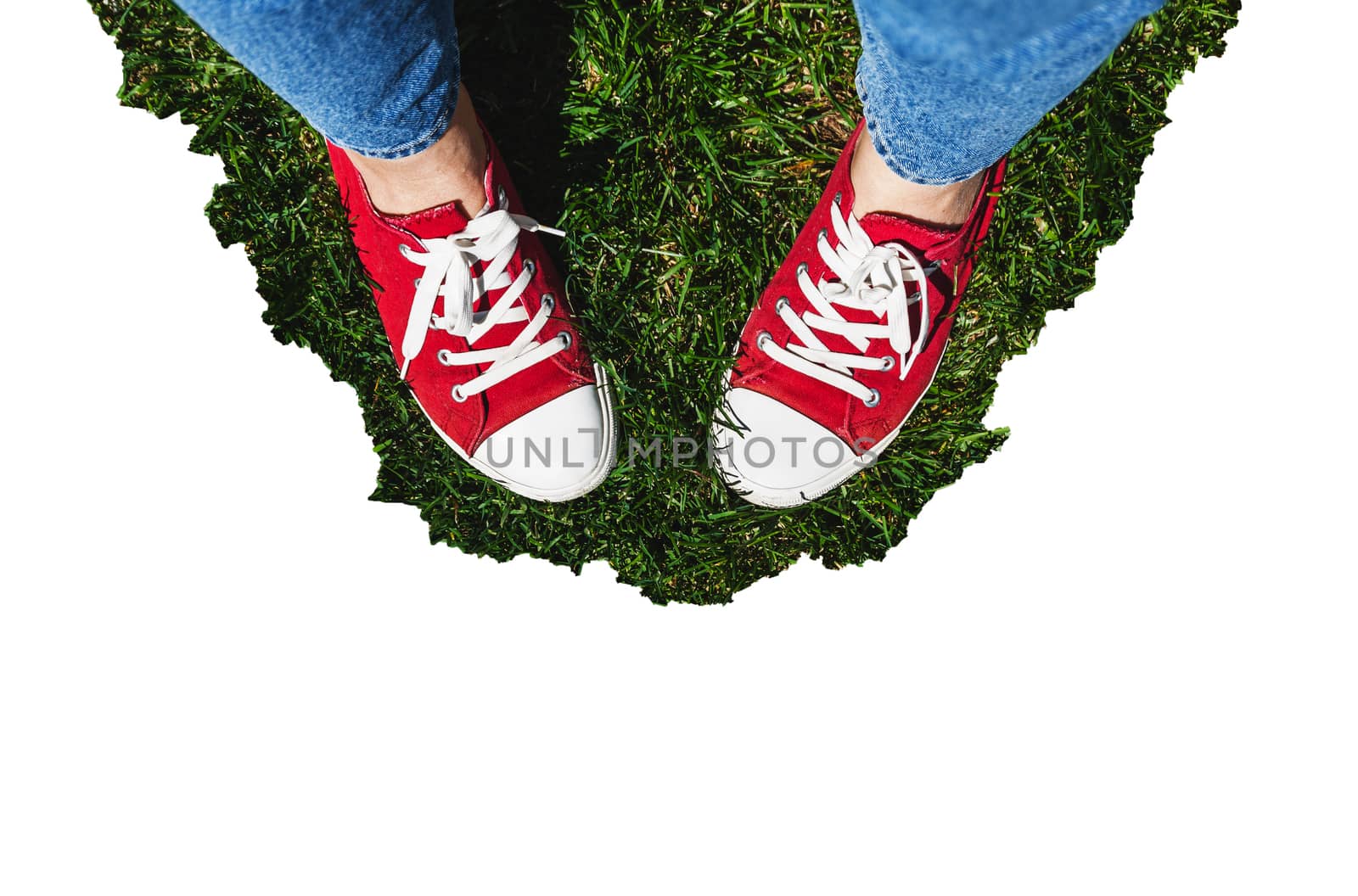 Legs in old red sneakers on green grass. View from above. The concept of youth, spring and freedom. Isolated on white background.