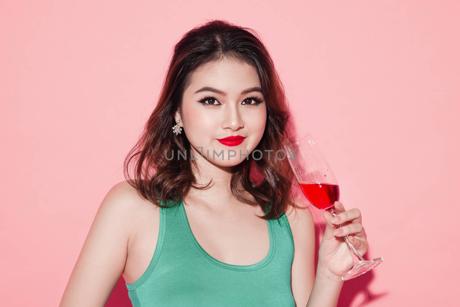 Happy fashion asian woman drinking champagne over pink background.