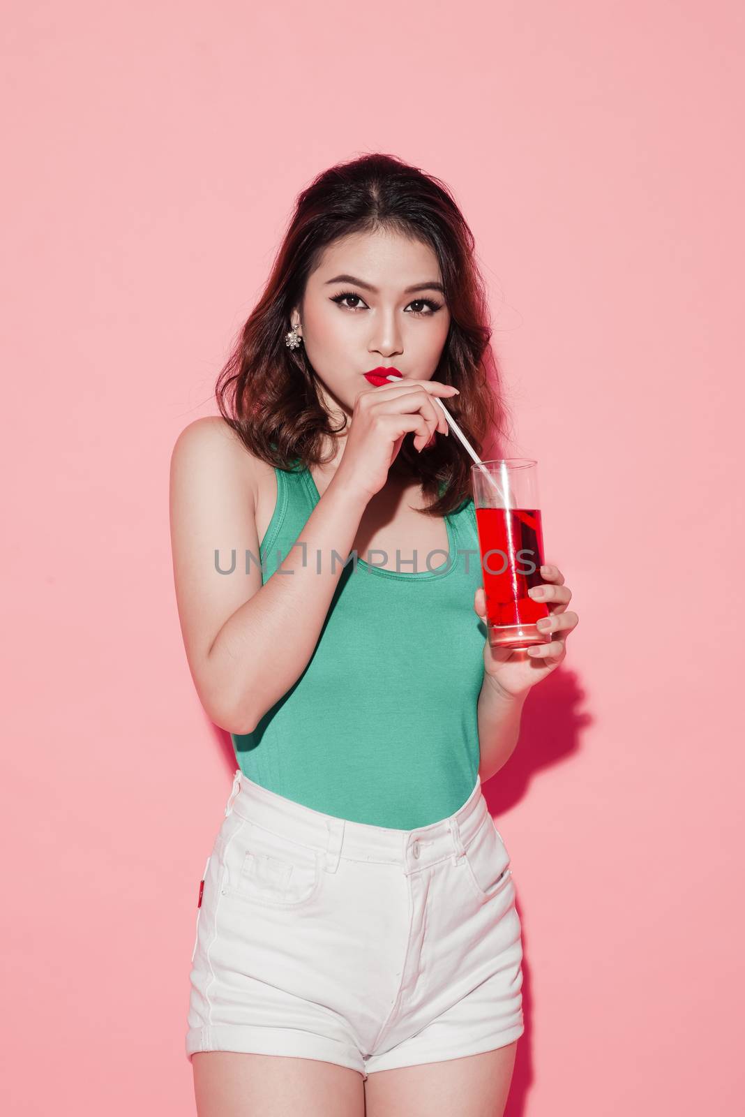 Happy fashion asian woman drinking champagne over pink background.