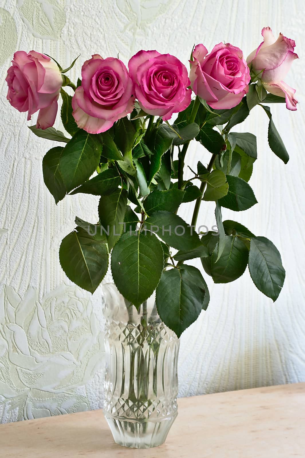A bouquet of pink roses stands in a vase on the table decorating the room.