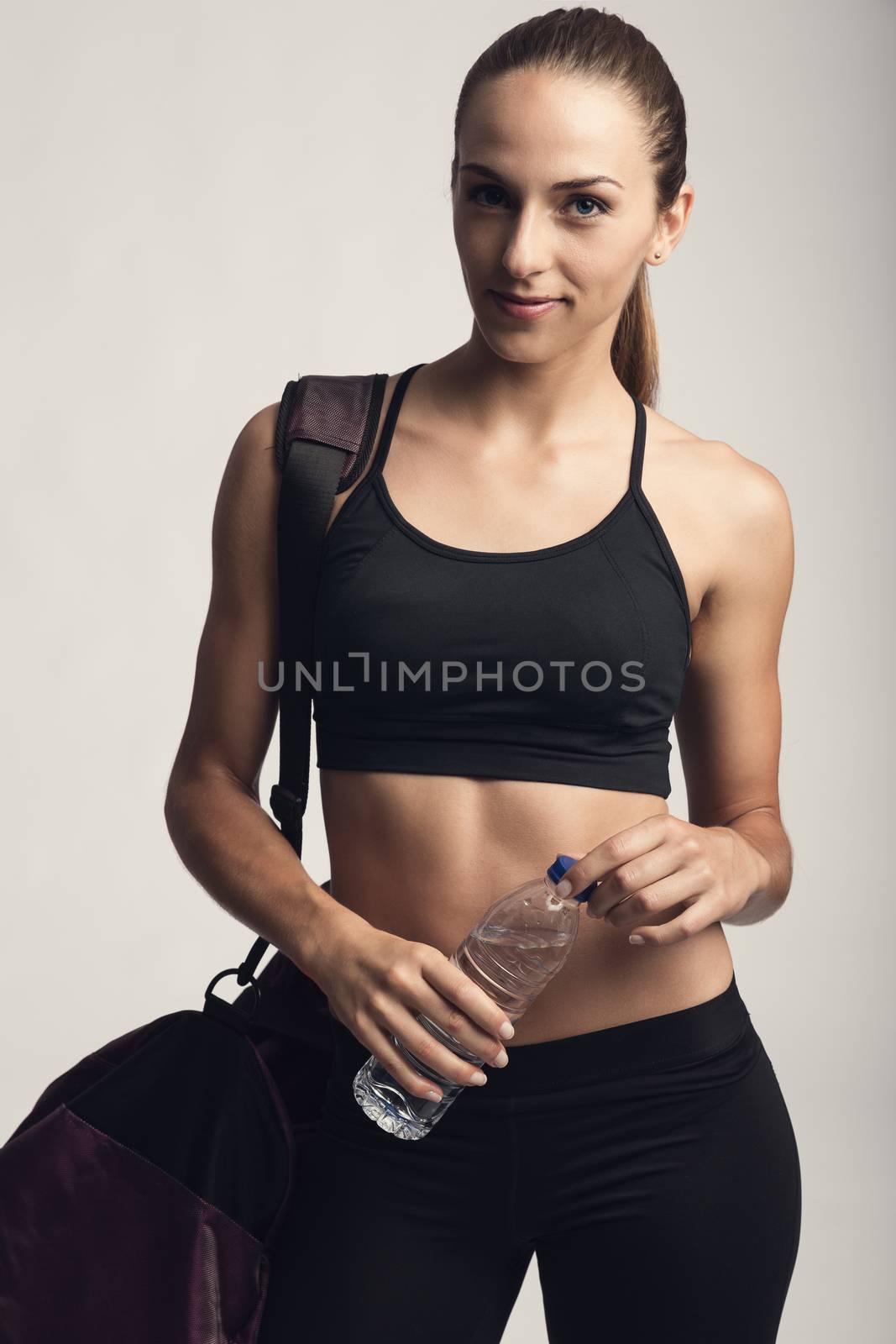 Portrait of sporty young woman posing with a gym bag and holding a water bottle