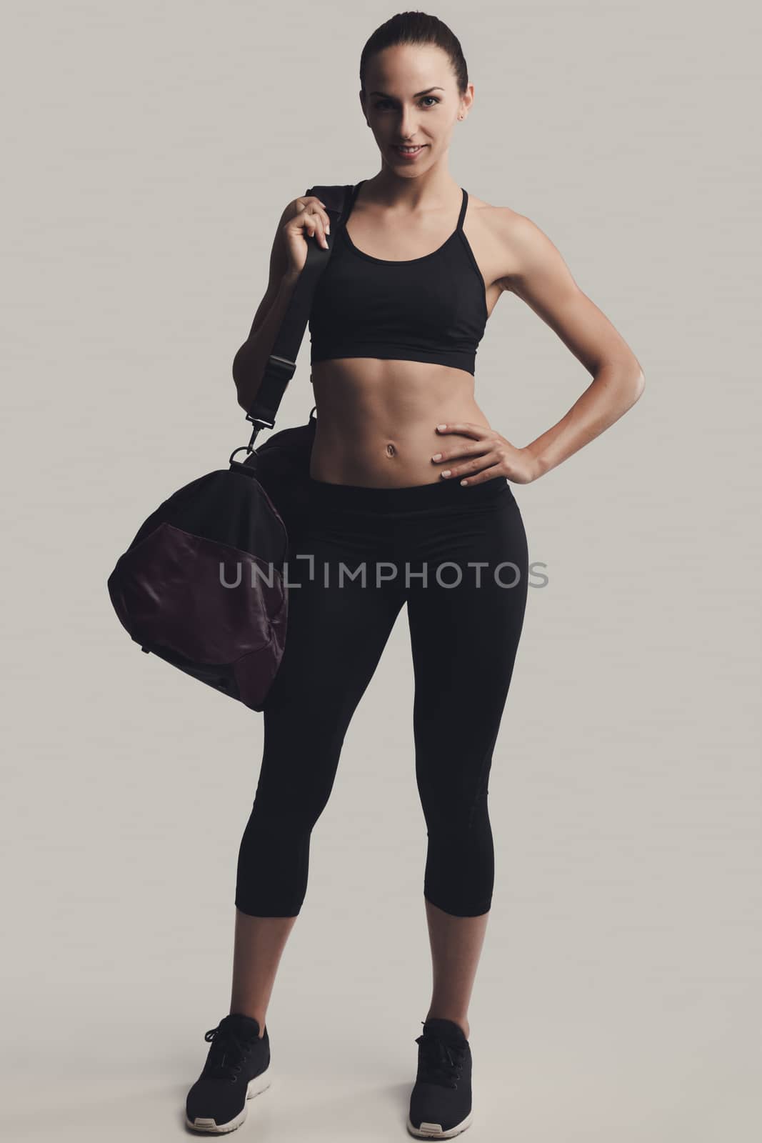 Portrait of sporty young woman posing with a gym bag,  against a gray background