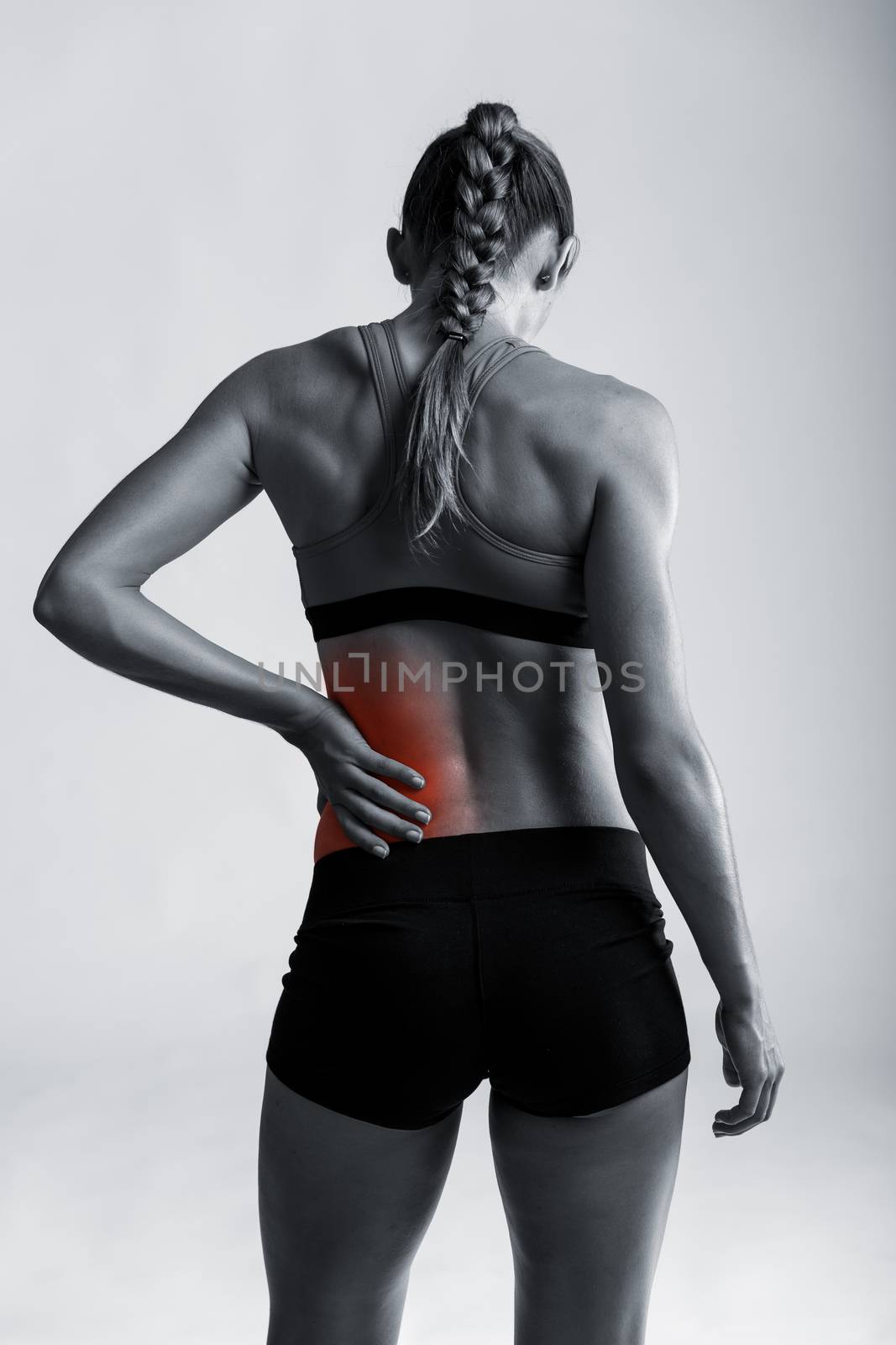 Studio shot of a sporty young woman holding her lower back in pain