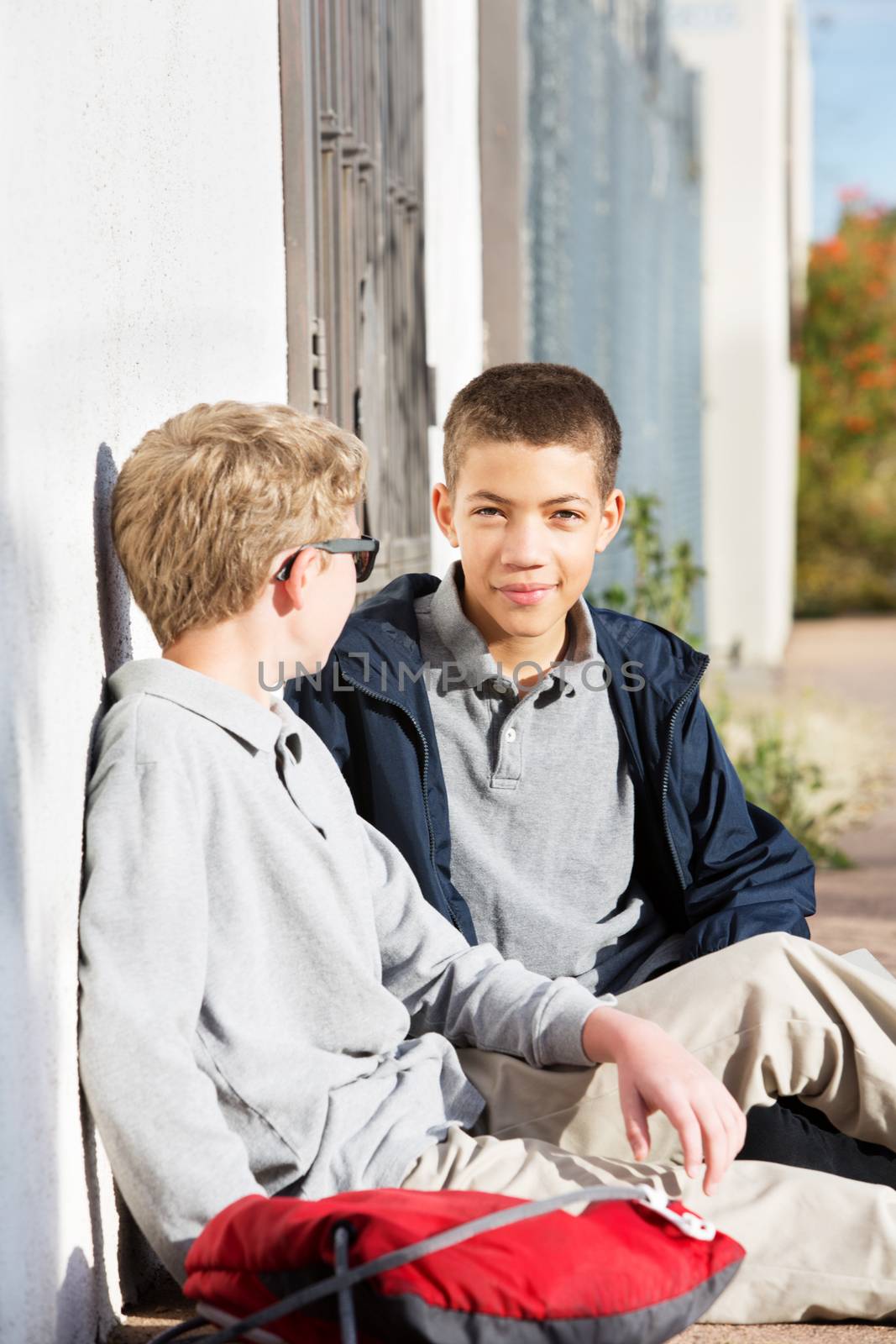 Two teenage youth sitting against wall together outdoors after school