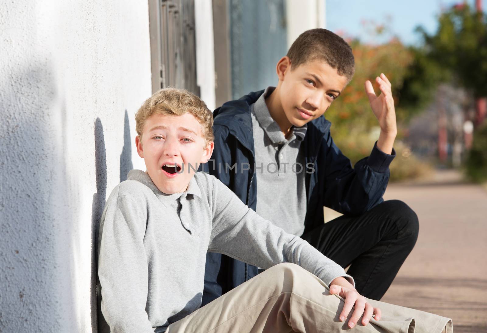 Embarrassed teen sitting next to yelling friend outside near wall
