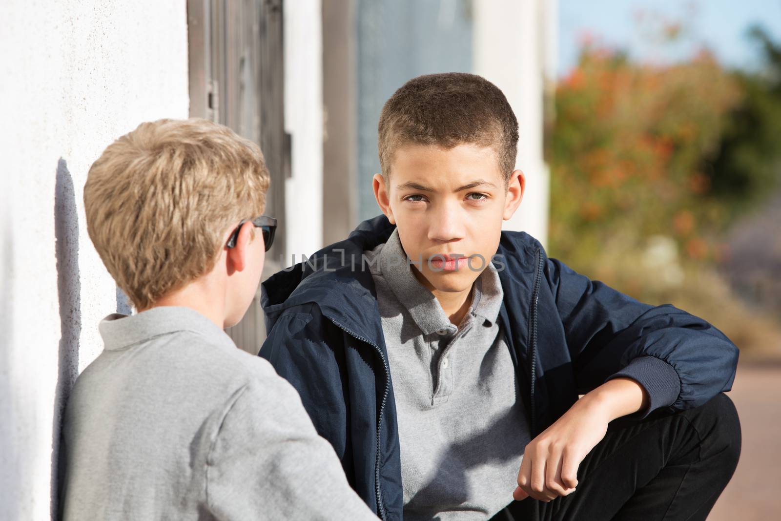 Male teen with serious expression listening to friend with blond hair talking outside