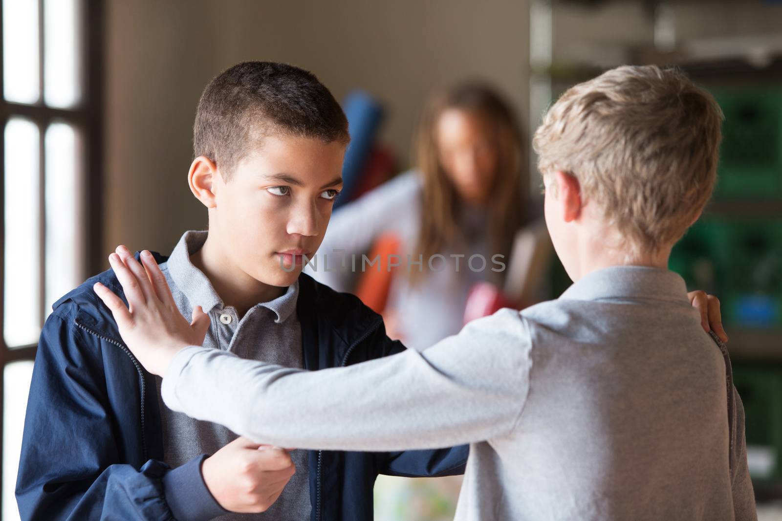 Black and white teenage male students fighting indoors. Obscured teacher in background.