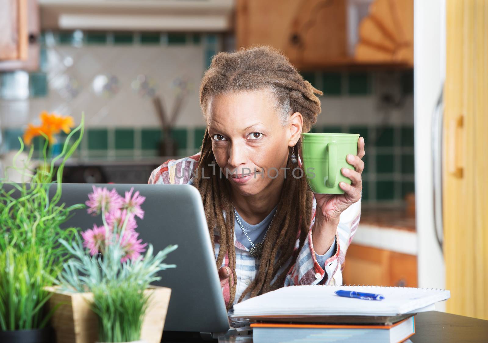 Grinning woman in kitchen with homework and laptop by Creatista