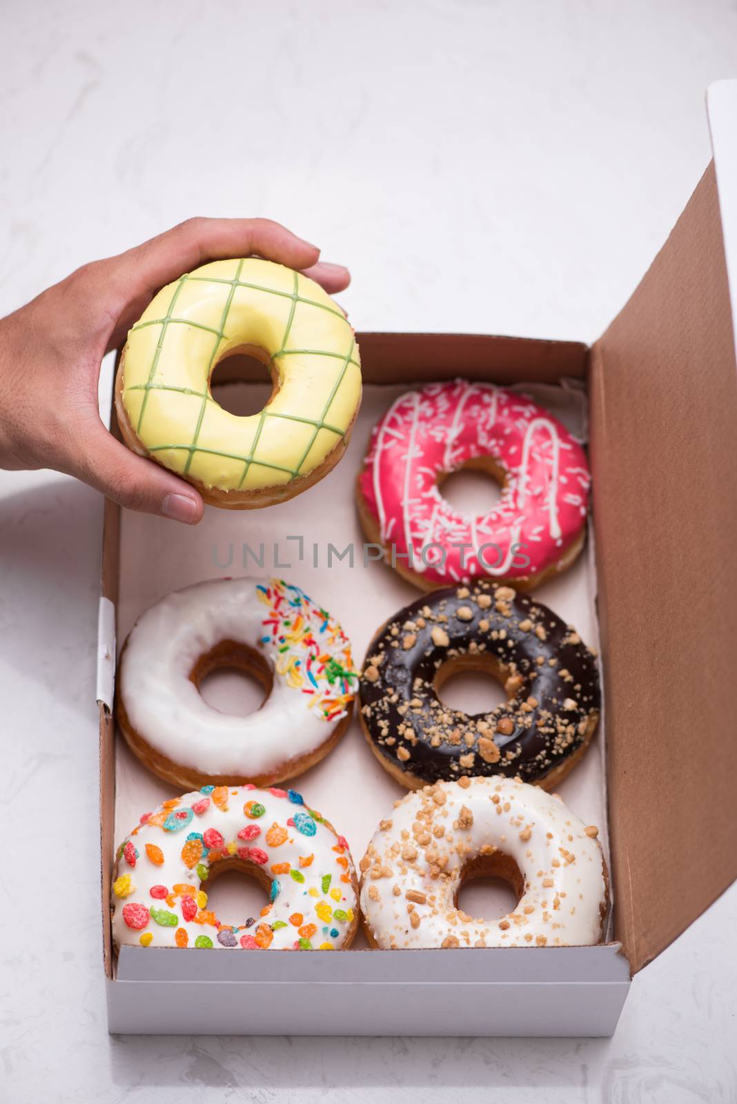 Hand holding colorful round donuts in the box