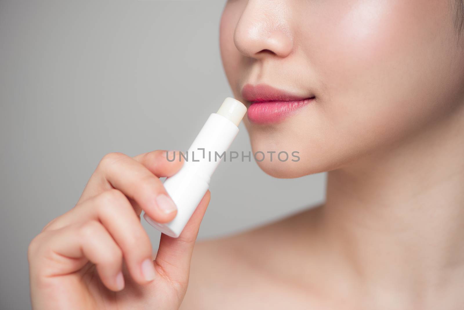 Asian woman applying hygienic lip balm over grey background