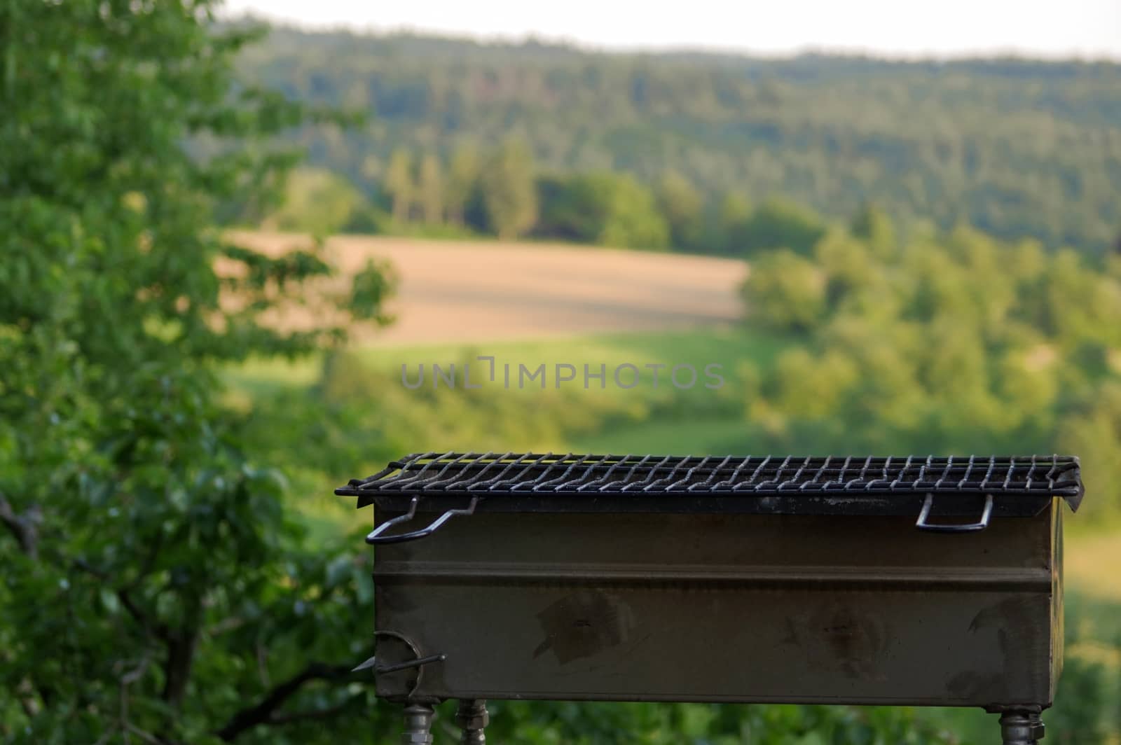 a empty portable BBQ grill in front of a fresh green summer landscape by evolutionnow