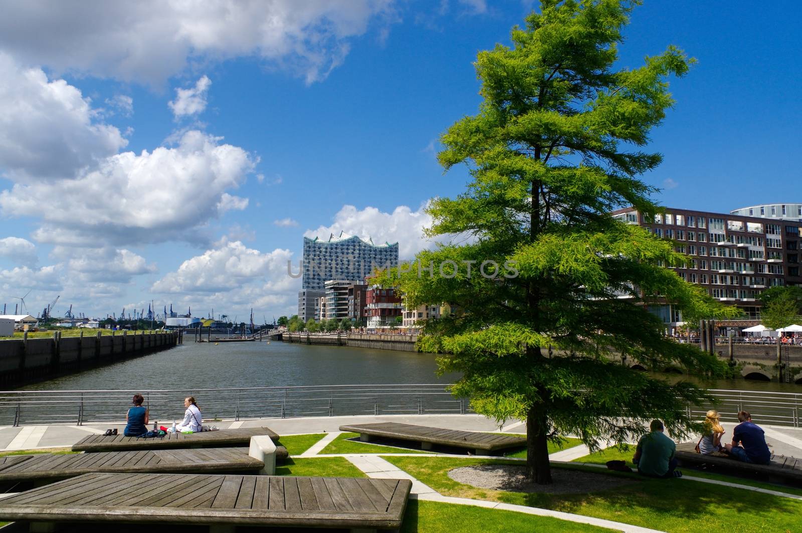 HAMBURG, GERMANY - JUNE 18, 2015: a little park with trees and resting peoples on beanches on the waterside by evolutionnow