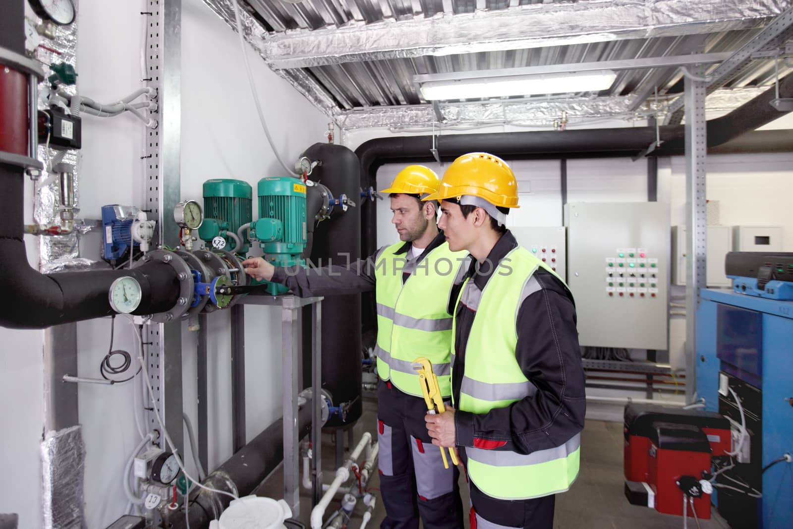 Two workers in hardhats at plant checking parameters of pressure