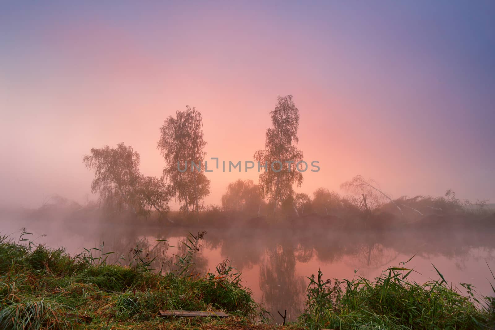 Autumn foggy morning. Colorful dawn on the misty calm river