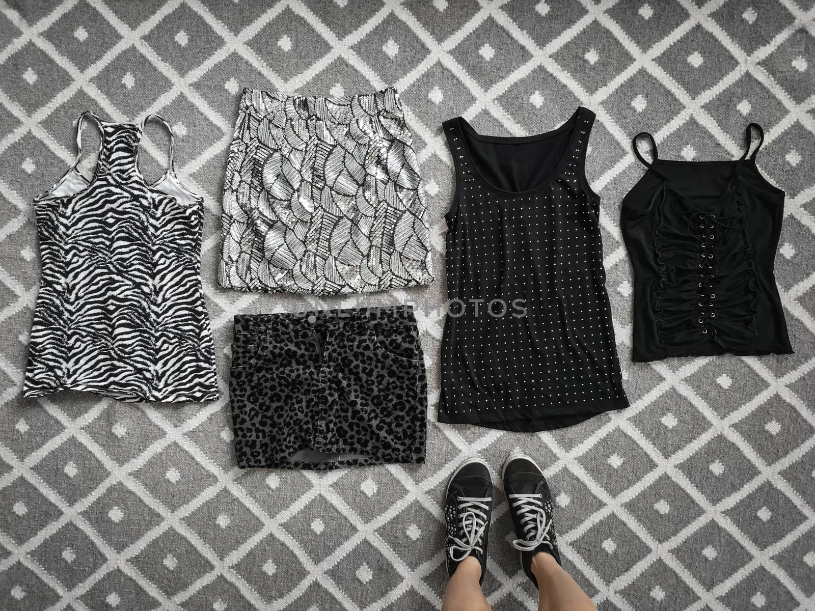 Choice of stylish black and white clothes on the floor, woman standing near it.