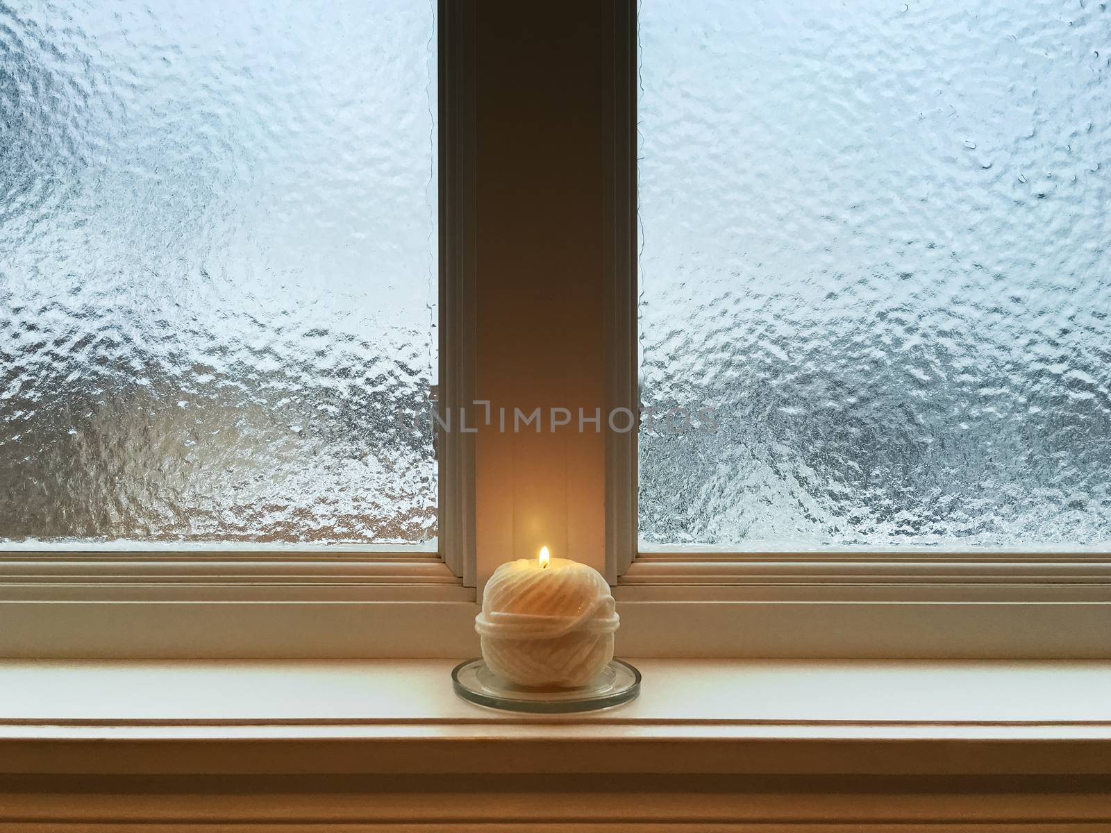 Candle on windowsill of a frosted window. Winter composition.