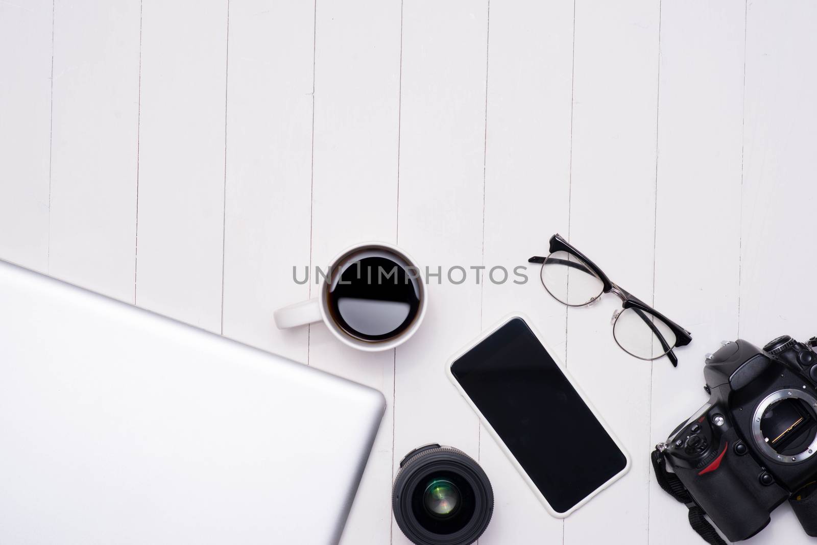 Flat lay photo of workspace desk with laptop, smartphone, coffee, eyeglasses and dslr camera