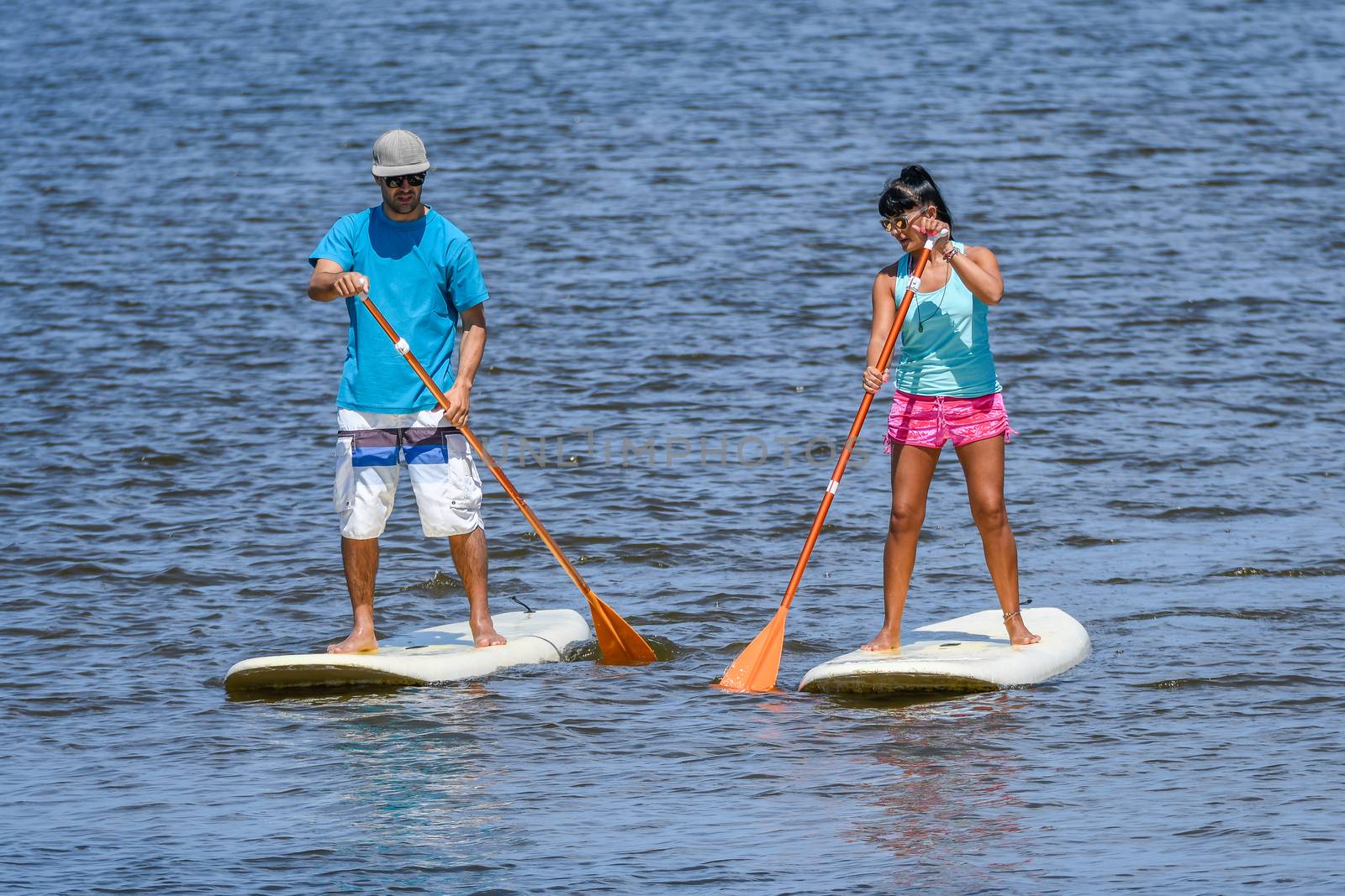 Man and woman stand up paddleboarding on lake. Young couple are doing watersport on lake. Male and female tourists are in swimwear during summer vacation.