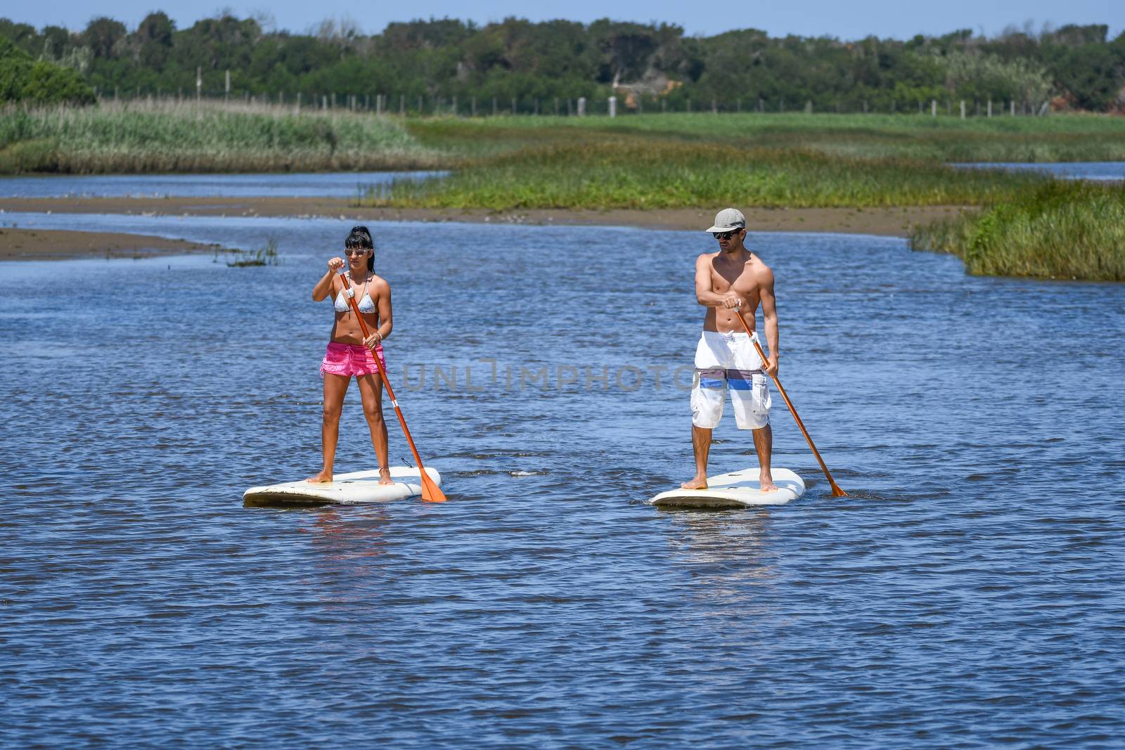 Man and woman stand up paddleboarding by homydesign