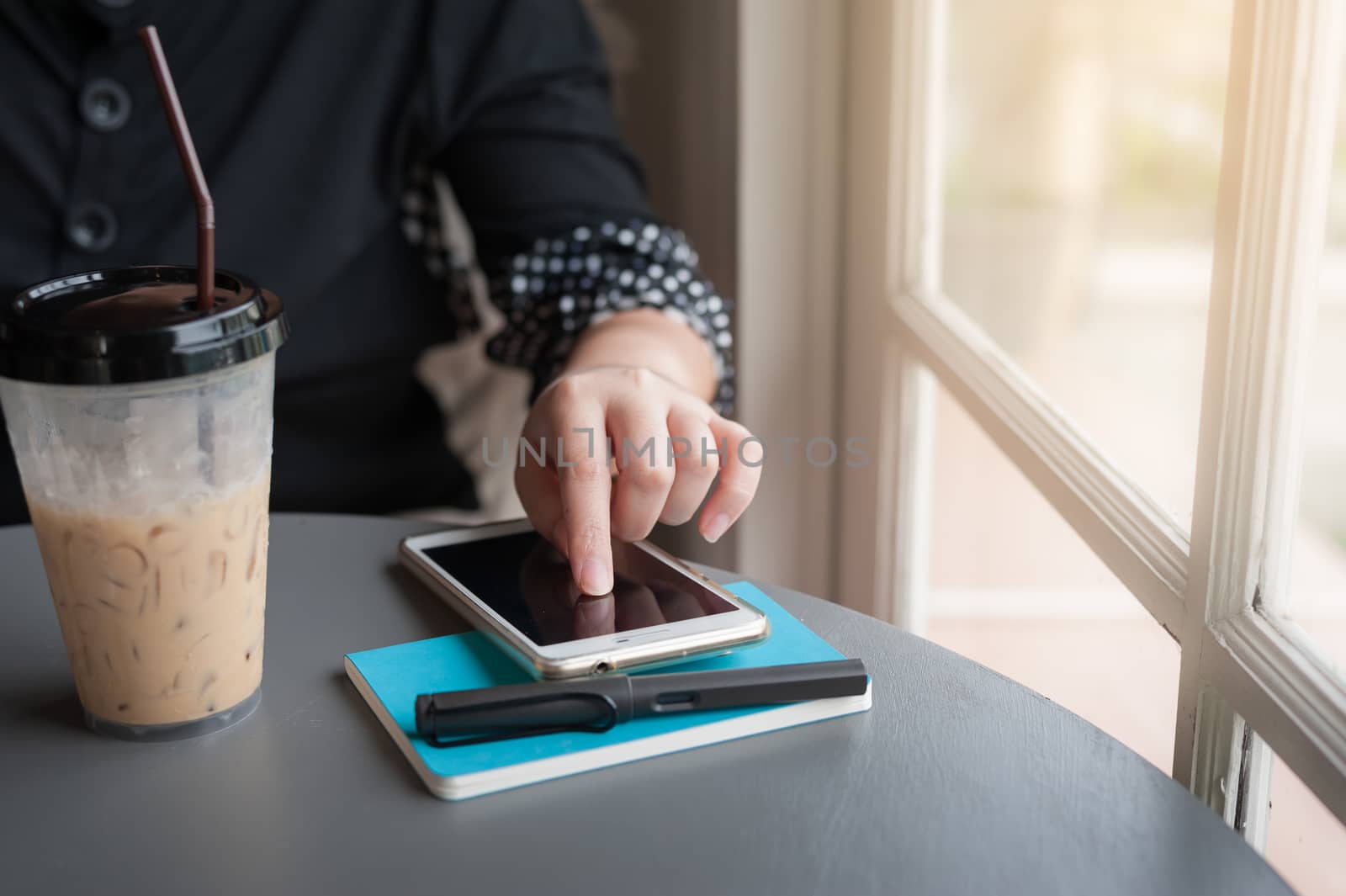 Woman using smartphone to check her agenda before writing a note to notebook in coffee shop. Freelance working from anywhere concept