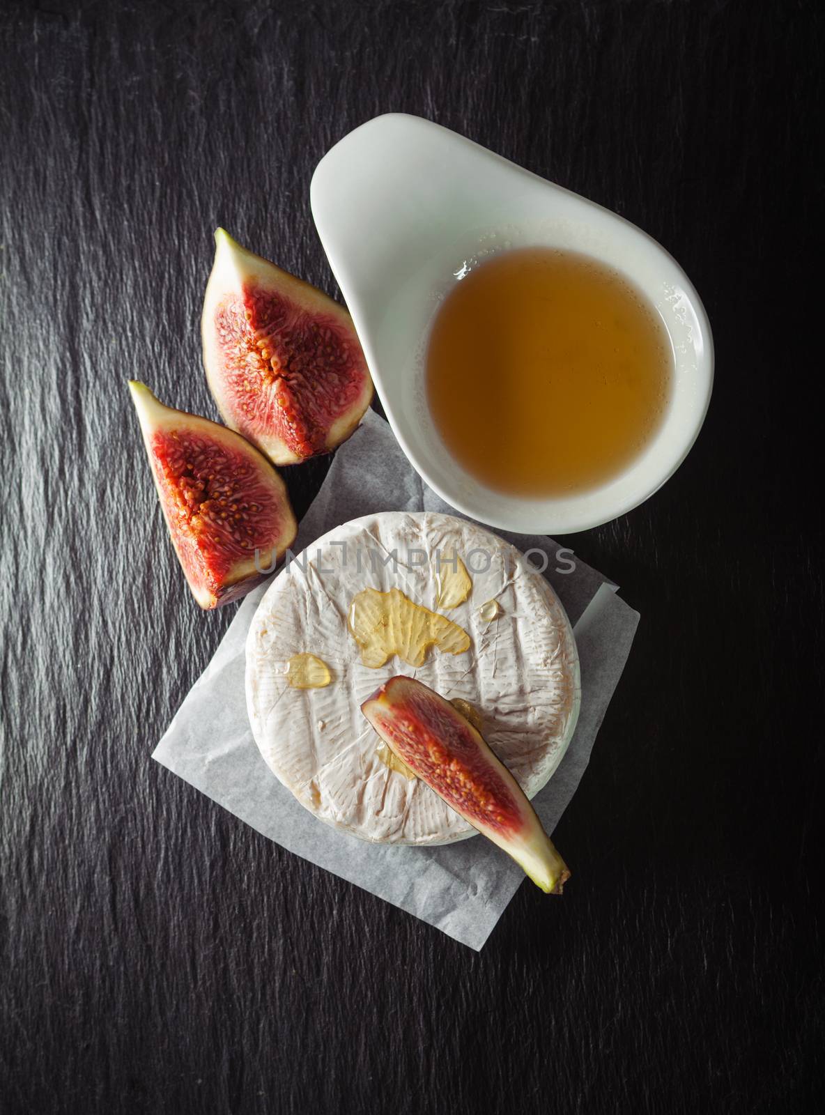 A wheel of melted brie covered in sliced figs and honey  on a stone plate.