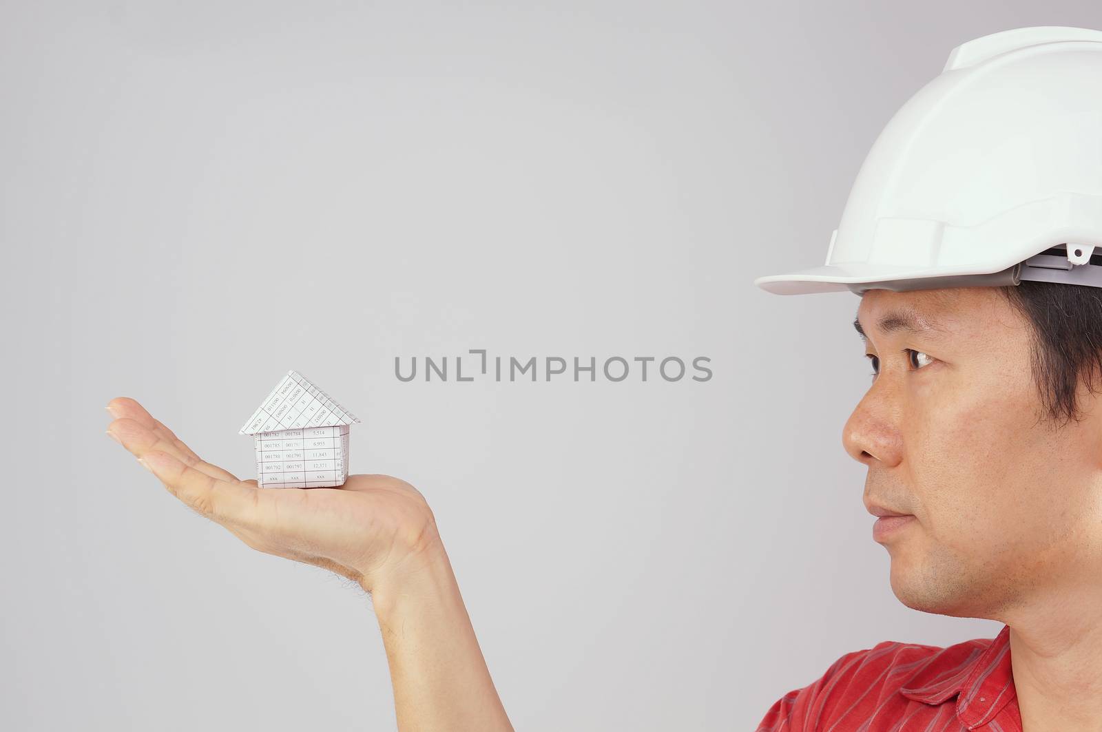 Engineer wear red shirt and white engineer hat is looking at house on hand with white background.