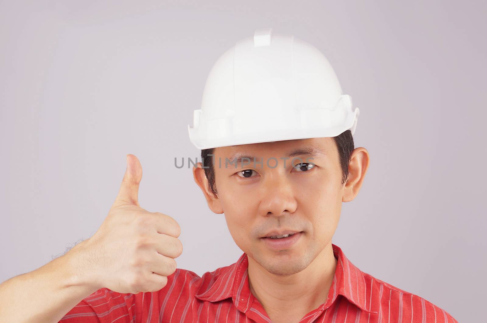 Engineer wear red shirt and white engineer hat make signal by thumb on white background.