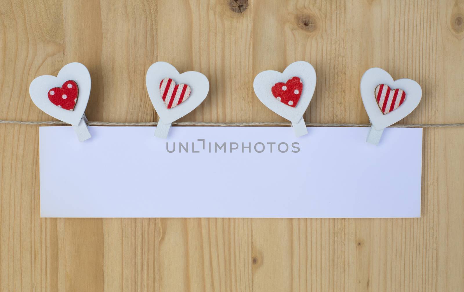 Four hearts with clothes pegs and paper on a cord on wood