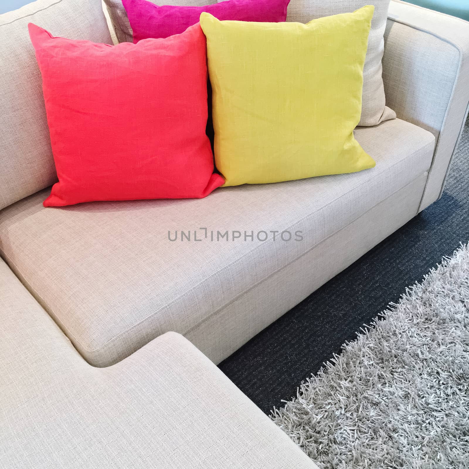 Bright pink and yellow cushions on a gray corner sofa.