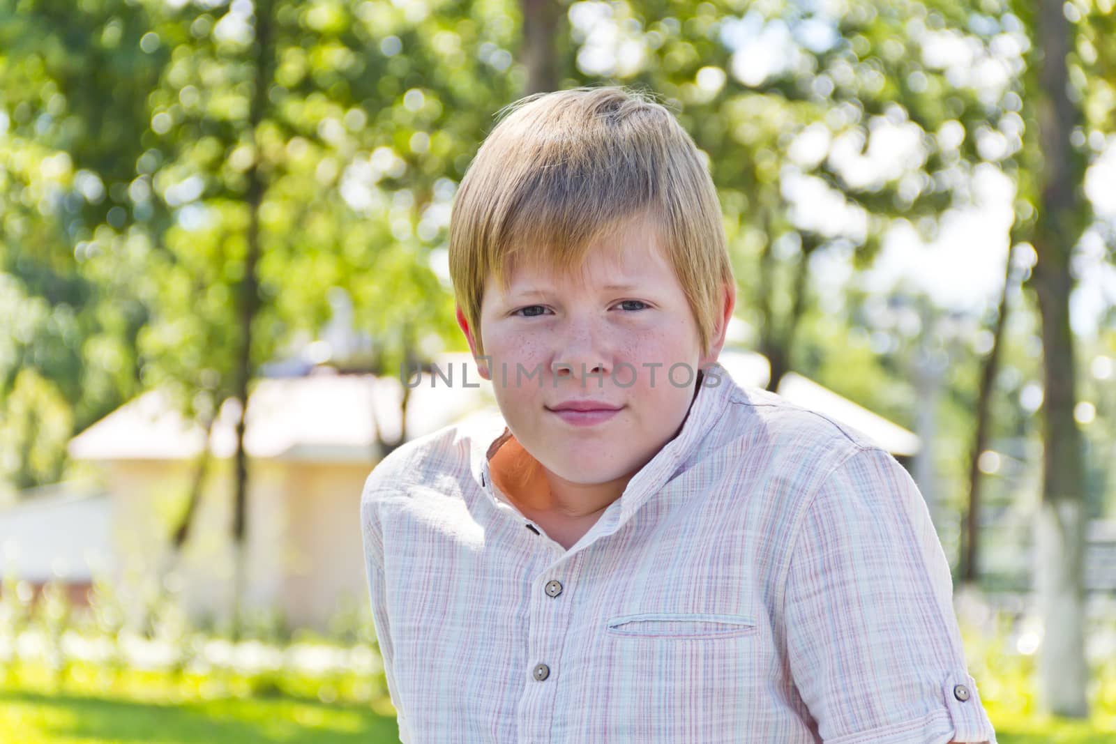 Portrait of  blond boy in a white shirt in green park