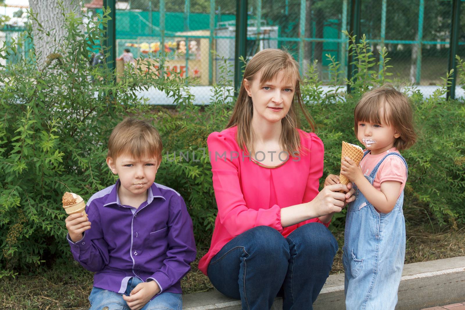 Mother with boy and baby girl sitting in summer park eating icecream