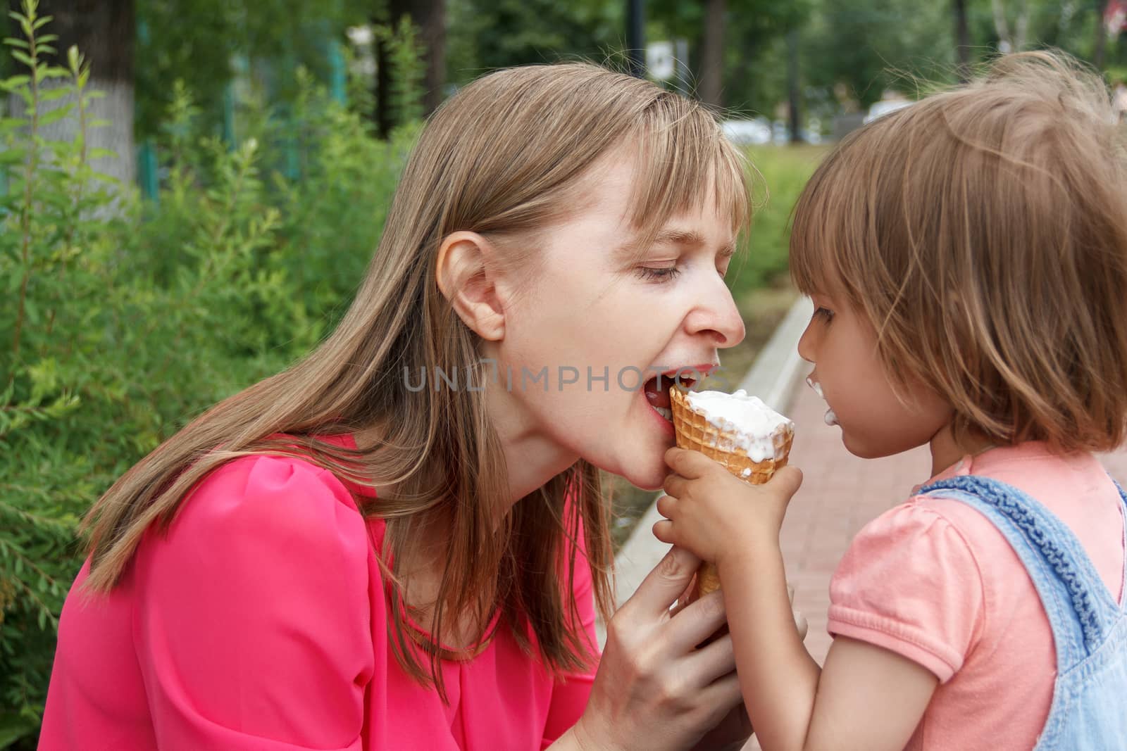 Mother and daughter in summer park are eating icecream