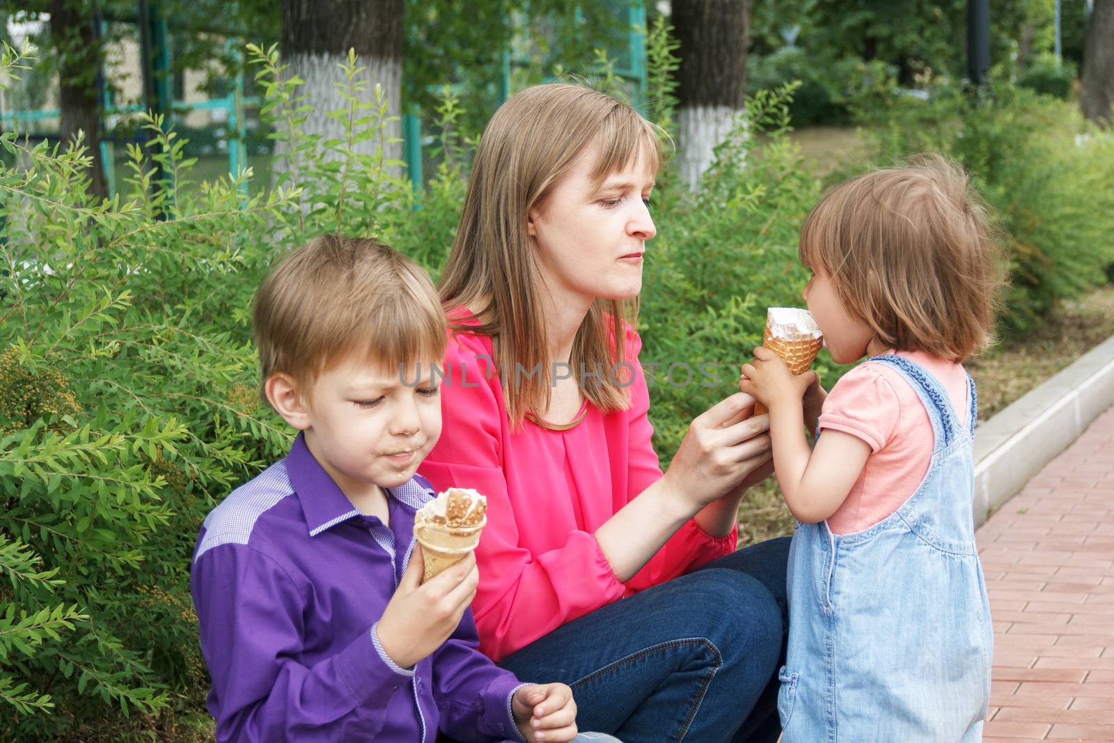 Mother with boy and baby girl sitting in summer park eating icecream