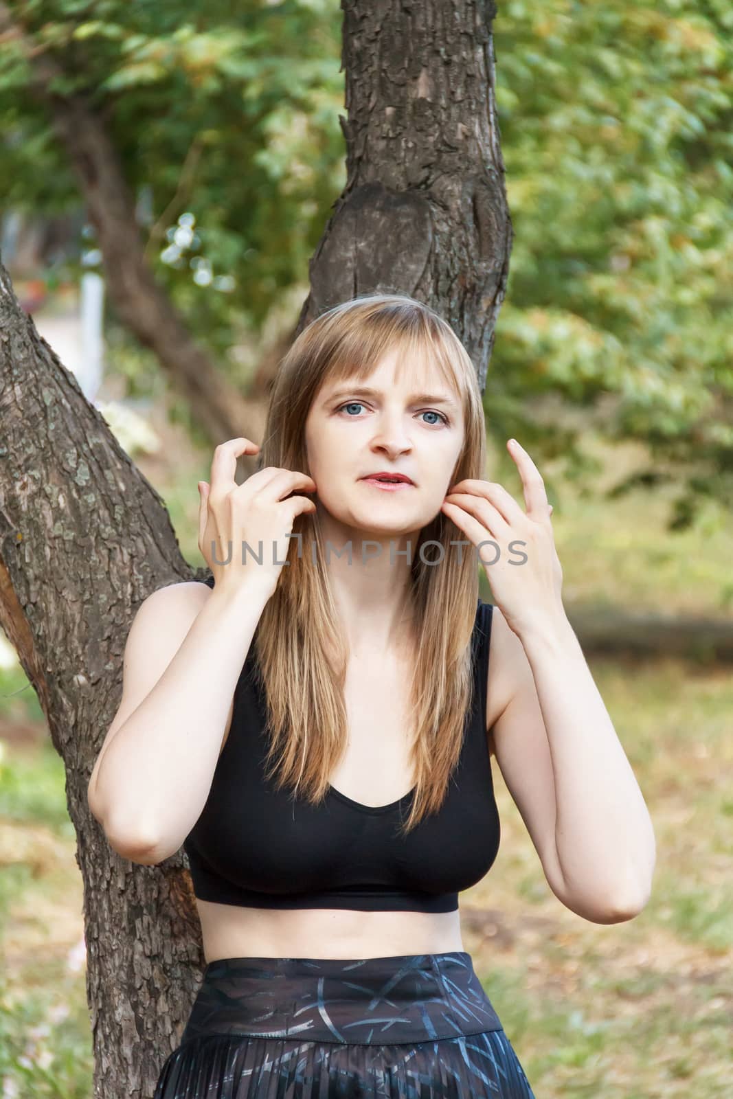 Beautiful blond woman corrects hair near tree in summer