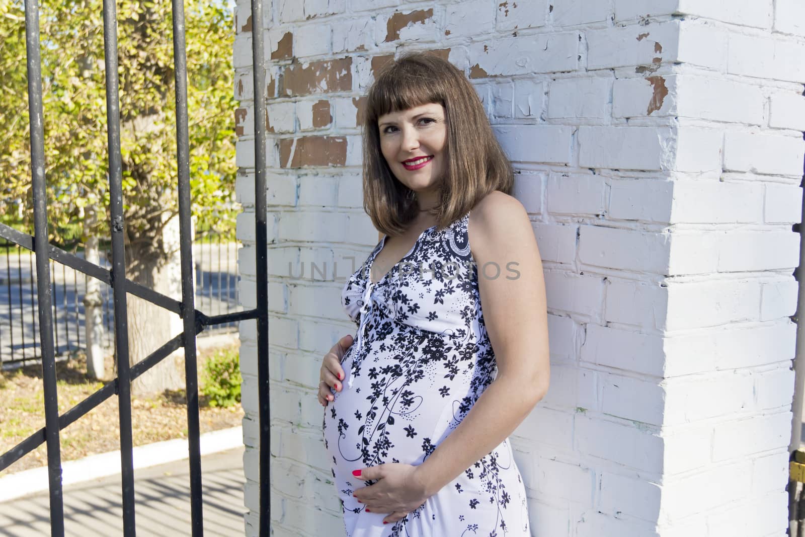 Pregnant woman with brown hair near white brick wall in summer