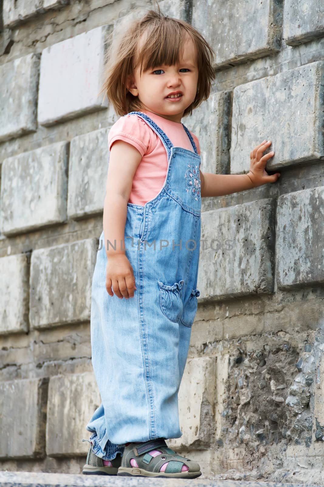 Baby girl in blue cloth standing near stone wall