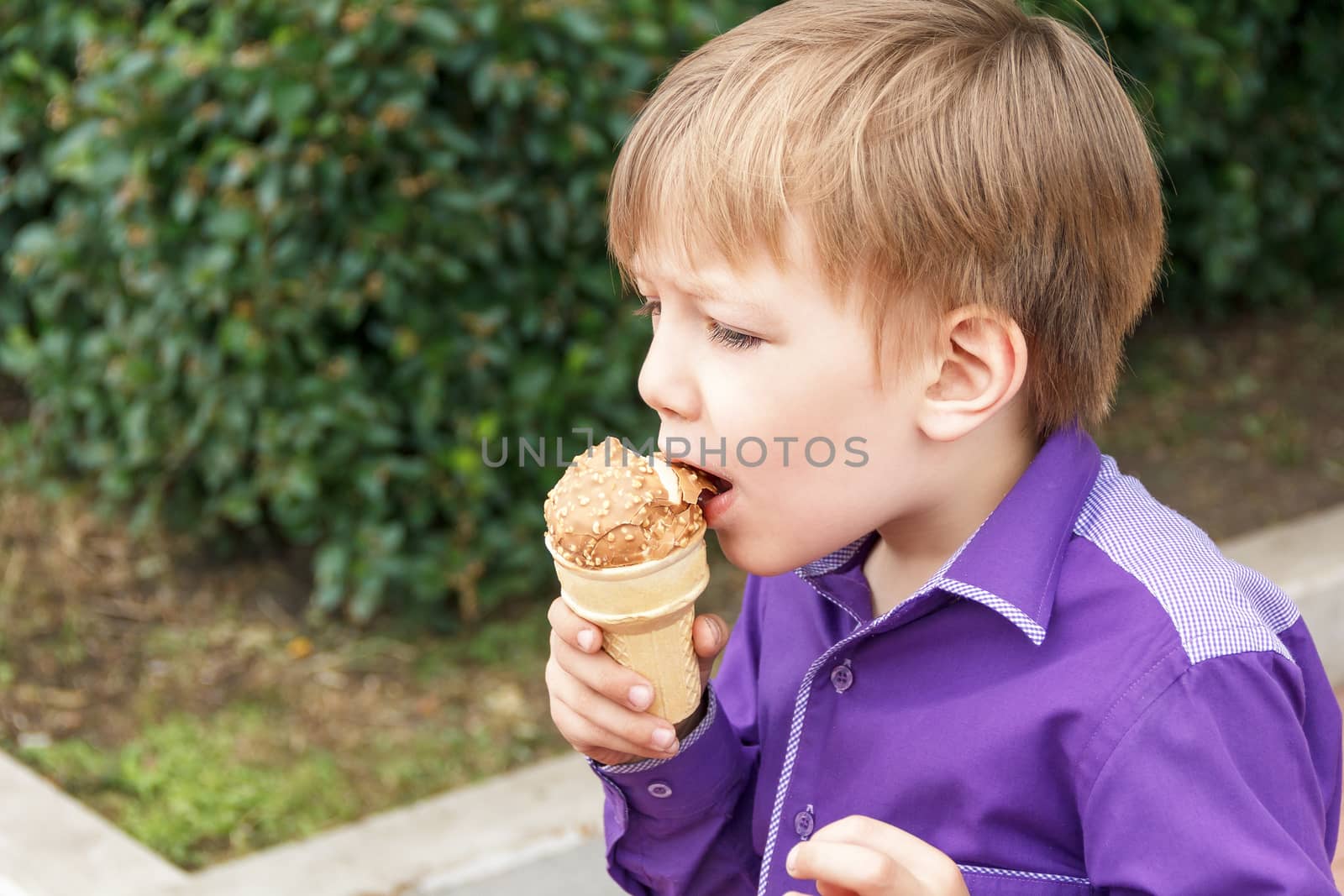 Horizontal photo of blond boy are eating icecream in summer