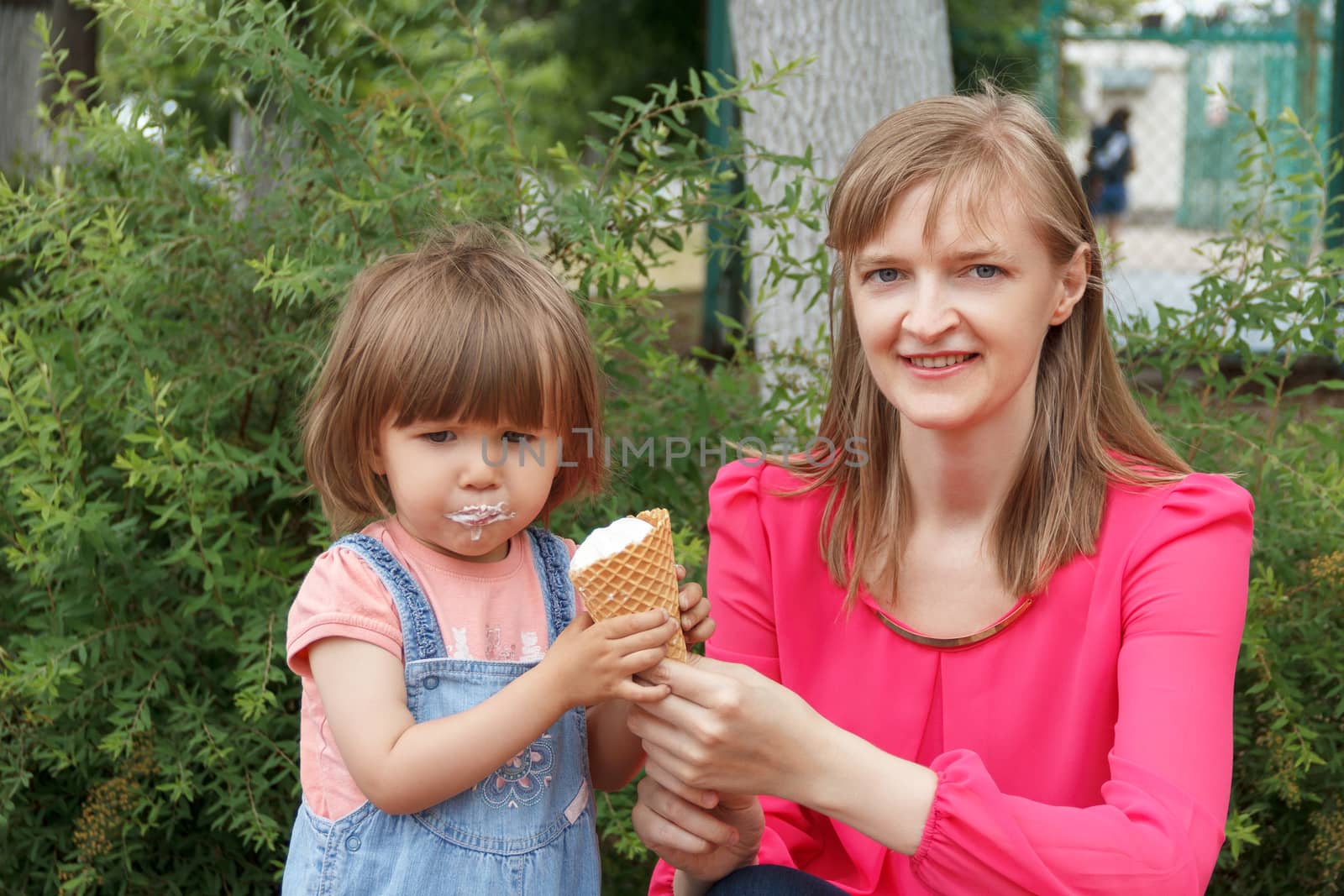 Mother and daughter in summer park are eating icecream