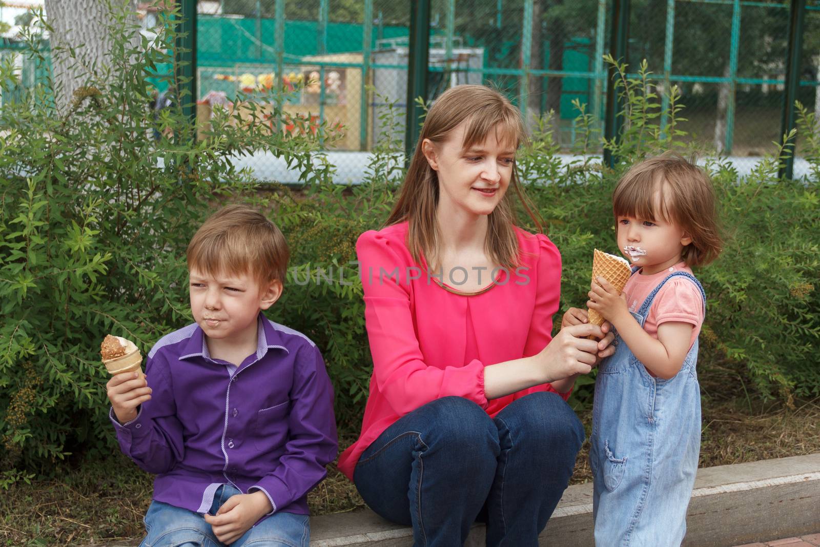 Mother with boy and baby girl sitting in summer park eating icecream